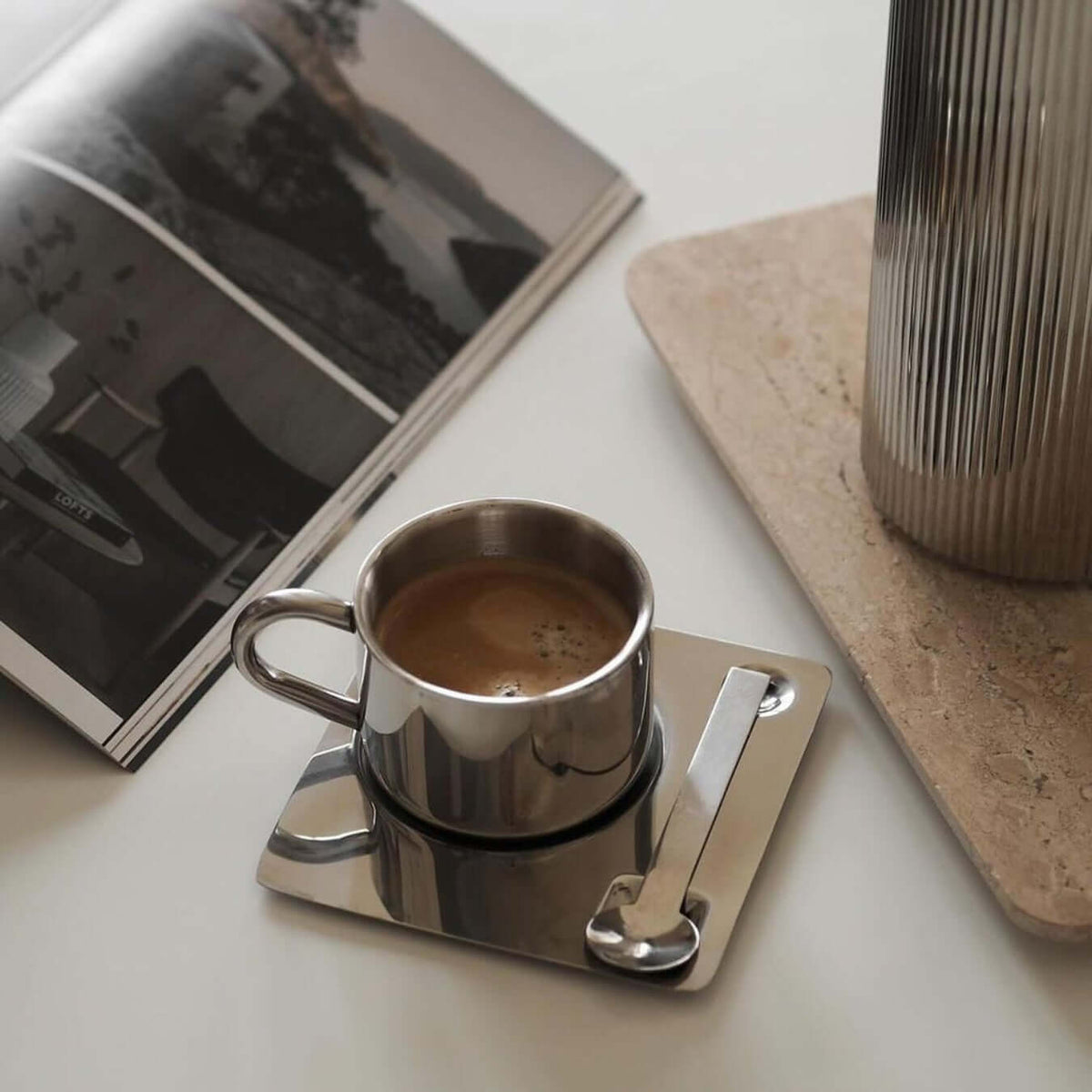Silberfarbene Tasse mit Untertasse und Löffel in spiegelnder Optik