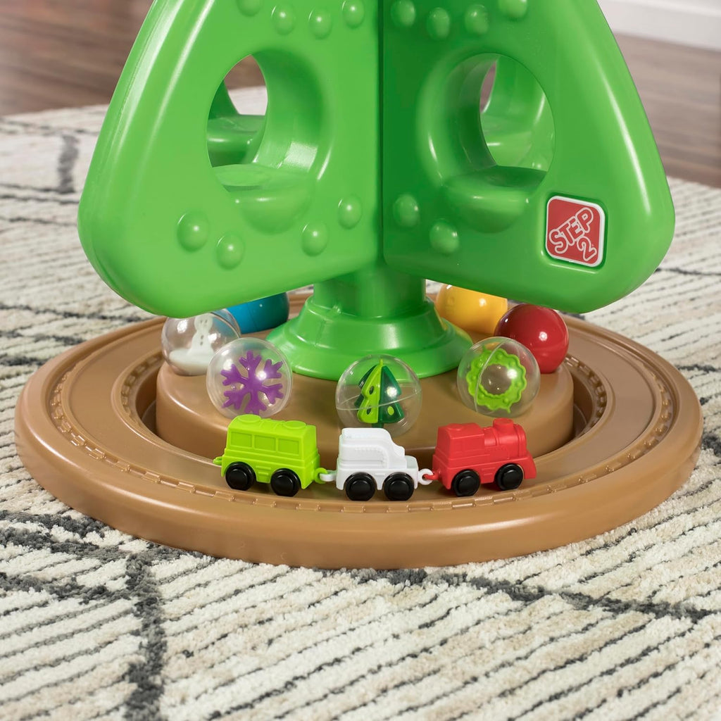 Grüner interaktiver Weihnachtsbaum mit bunten Spielelementen und kleiner Spielzeugeisenbahn