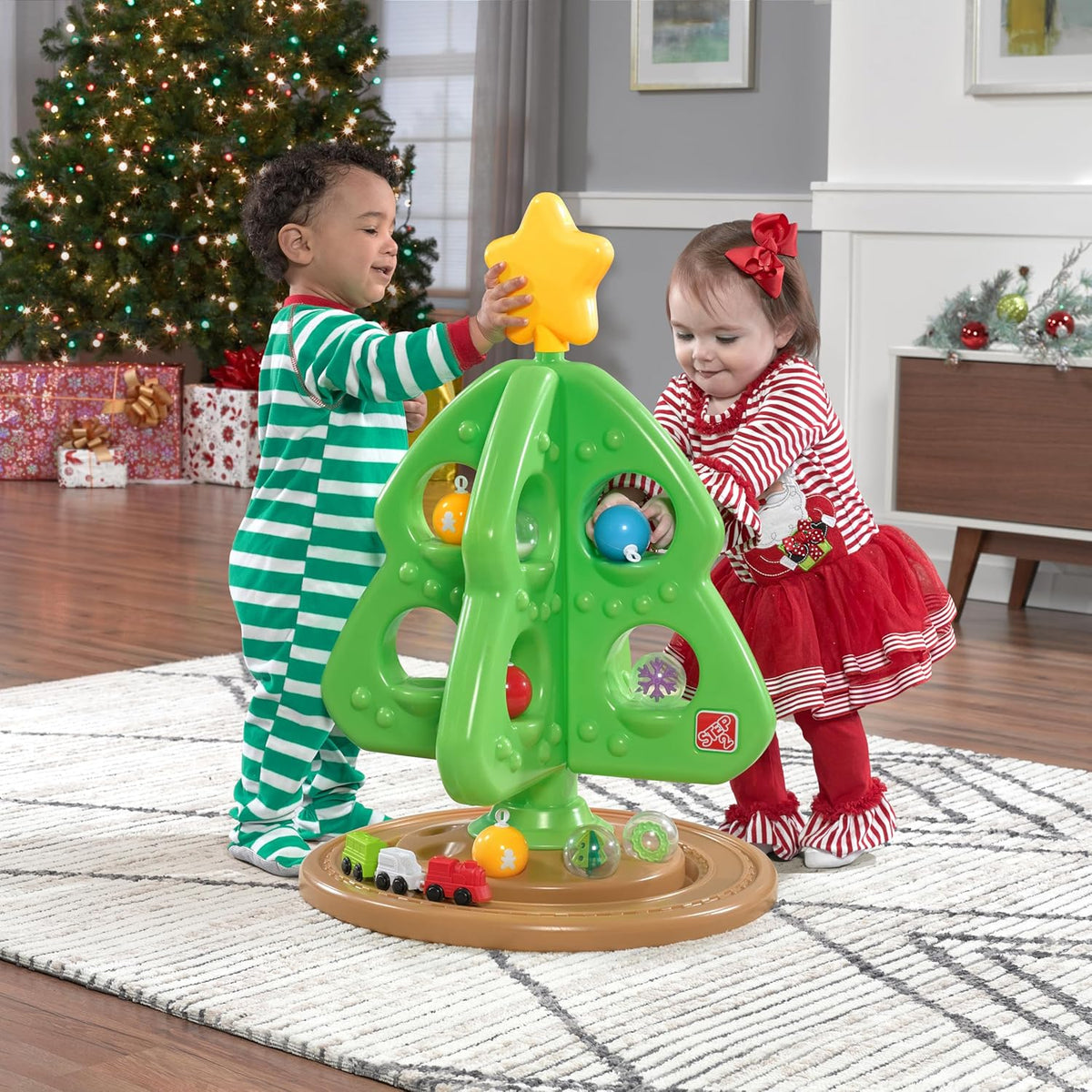 Grüner interaktiver Weihnachtsbaum mit bunten Spielelementen und kleiner Spielzeugeisenbahn