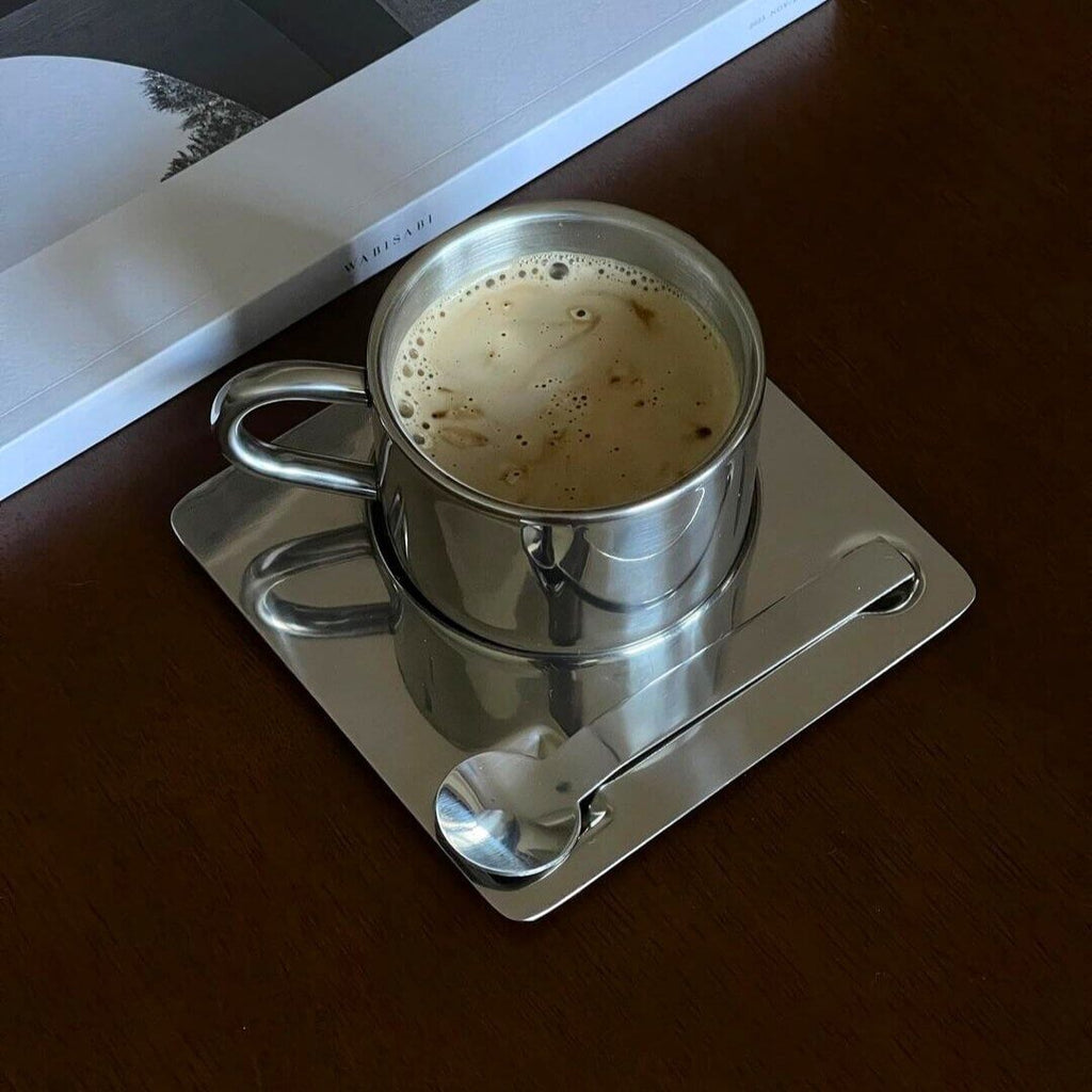 Silberfarbene Tasse mit Untertasse und Löffel in spiegelnder Optik