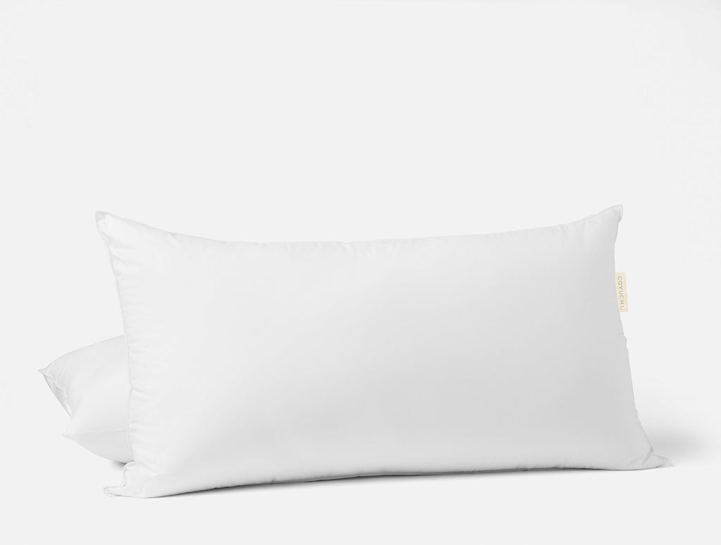 Weißes Kopfkissen mit Daunenfedern auf einem Bett